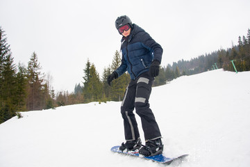 A young man in sports glasses and in the helmet is riding a snowboard in the mountains in Transcarpathia