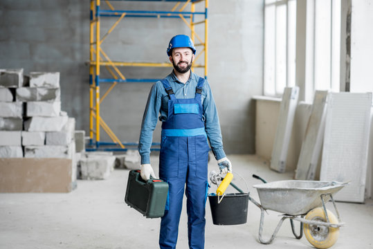 Builder in working uniform with protective helmet standing with instruments at the construction site indoors