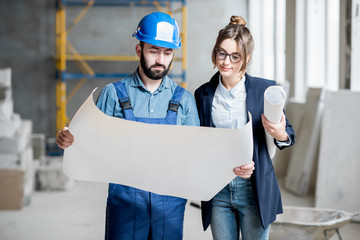 Foreman expertising the structure with businesswoman holding a blueprints at the construction site indoors