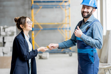 Businesswoman giving cryptocoin to builder as a salary for the work standing at the construction...