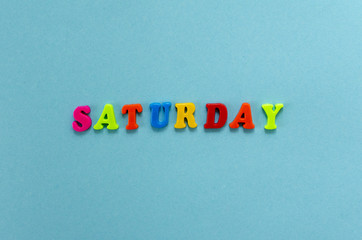 word "saturday" of colored plastic magnetic letters on blue paper background
