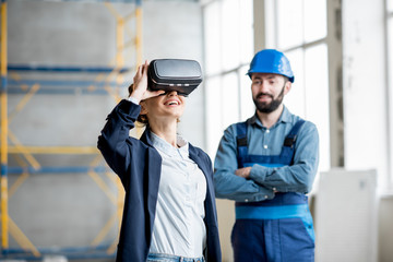 Woman client wearing VR glasses imagining future interior standing with builder at the construction...
