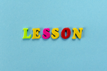 word "lesson" of colored plastic magnetic letters on blue paper background