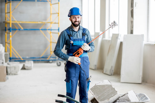 Portrait of a builder in working uniform standing with drill at the construction site indoors