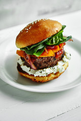 Burgers with grilled beef patties, cream cheese and spinach on classical bun. White wooden background