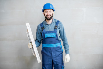 Portrait of a handsome builder in blue working uniform plastering the wall indoors