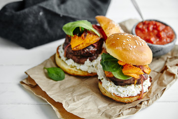 Burgers with grilled beef patties, cream cheese and spinach on classical bun. White wooden background