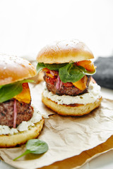 Burgers with grilled beef patties, cream cheese and spinach on classical bun. White wooden background