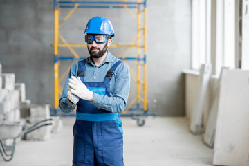 Close-up portrait of a handsome bearded builder with protective glasses and helmet indoors