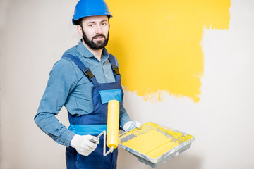 Portrait of a handsome painter in working uniform painting wall with yellow paint