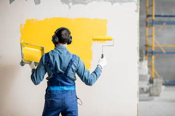 Happy repairman listening to the music with headphones during the painting wall indoors