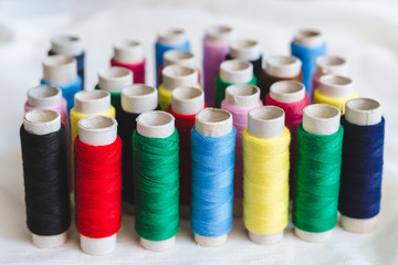 Group of colored thread spools on white cotton cloth