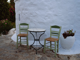 Small traditional green wooden chairs and a black metallic table next to a chapel