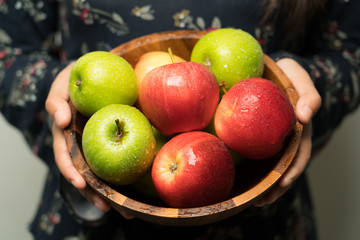A woman holding a cup filled with apples.
