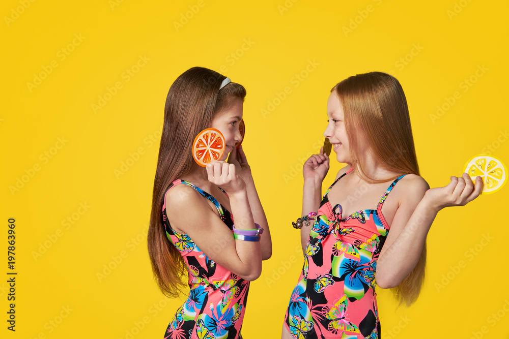 Wall mural portrait two cheerful girlfriends in colorful swimsuits looking at each other,holding image citrus.c