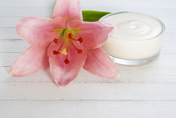 Cosmetic cream and lily flower on white wooden table