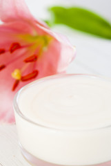 Cosmetic cream and lily flower on white wooden table
