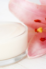 Cosmetic cream and lily flower on white wooden table