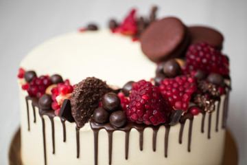 cake with white cream, chocolate drips, pomegranate, nuts and chocolate decor