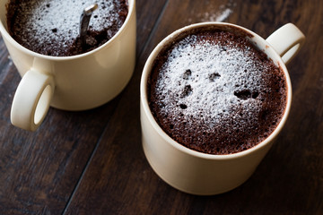 Microwave Brownie Chocolate Mug Cake with Powder Sugar on Dark Wooden Surface.