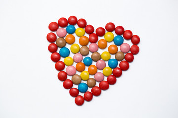 Colorful m&m button chocolate candies in the love shape on white background.