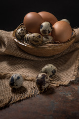 Chicken and quail eggs in bowl on rustic wooden background