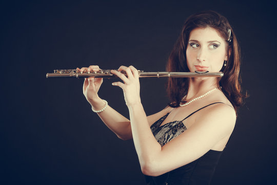 Woman playing transverse flute on black.