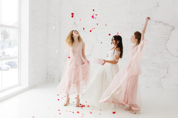 Bride and bridesmaids dancing in white loft studio with flying petals. Full-lenght portrait