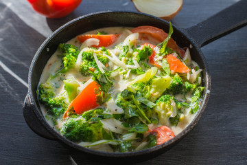 Mixed raw eggs, broccoli and tomatoes and vegetables in a frying pan - cooking omelette tomatoes