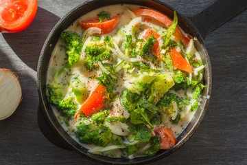 Mixed raw eggs, broccoli and tomatoes and vegetables in a frying pan - cooking omelette tomatoes
