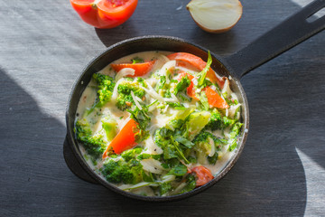Mixed raw eggs, broccoli and tomatoes and vegetables in a frying pan - cooking omelette tomatoes