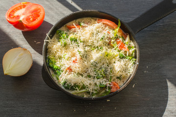 Mixed raw eggs, broccoli and tomatoes and vegetables sprinkled with cheese in a frying pan - cooking omelet