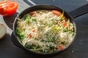Mixed raw eggs, broccoli and tomatoes and vegetables sprinkled with cheese in a frying pan - cooking omelet