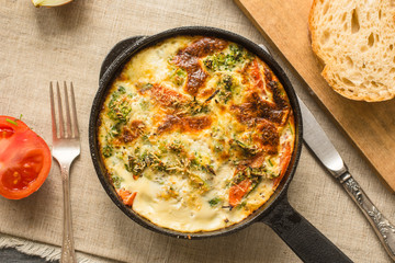 Traditional Italian omelette with broccoli and tomatoes in a frying pan on a rustic background