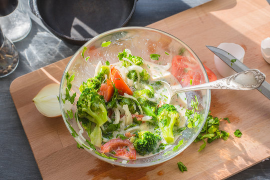 Mixed raw eggs, Broccoli and tomatoes and vegetables in a glass bowl - cooking omelette