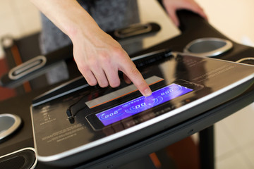 Young man athlete exercising on treadmill in modern gym, setting up difficulty level