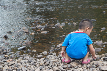 baby boy child playing outside in the river near a waterfall in the forest  dangerous do not leave children unattended near the water alone