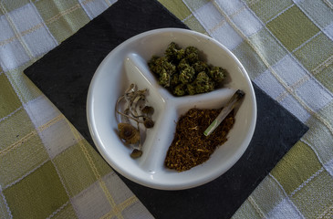 Plate with three drugs: marijuana (with joint), shopped tobacco and magic mushroom. Beautiful presentation with black rock tray.