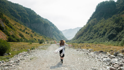 A girl in a hat walks along the middle of the road towards the mountains 