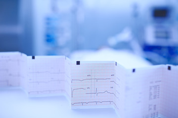 ECG chart accordion-folded on the nurse's table on the background of patient lying in his bed