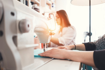 Naklejka premium Closeup photo of young woman's hands seamstress sitting and sews on sewing machine in creative designer studio. Two young businesswoman dressmaker making new clothing