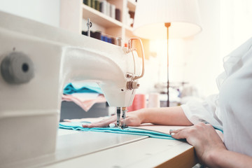 Young woman dressmaker working on sewing machine in sew showroom. Seamstress working with cloth in workshop. Small business