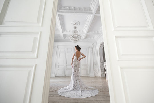 Beautiful bride posing in wedding dress in a white photo Studio. Mirror. Sofa. Bouquet. The door. Chandelier.