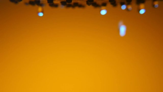 An abstract macro shot of brilliant water blods dribbling from a metallic shower nozzle in a bathroom with brown walls 