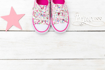 Pink baby sneakers and lettering on a white wooden background. Copy space