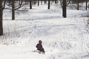 Fototapeta na wymiar child slipping on a toboggan from a hill in the winter forest. copyspace