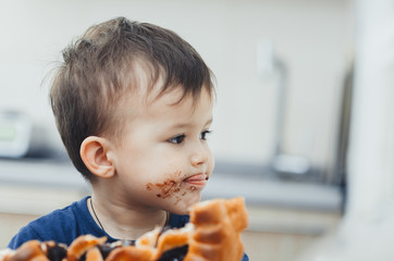 baby in the kitchen eating a big bun or pie with chocolate and condensed milk all dirty
