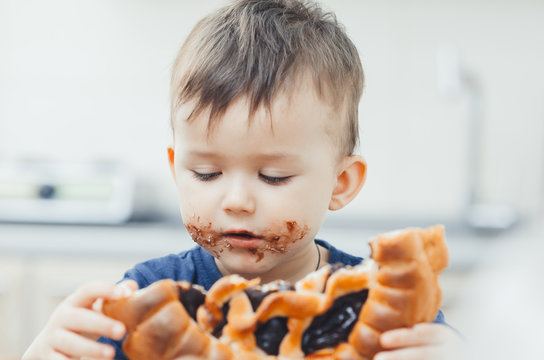 baby in the kitchen eating a big bun or pie with chocolate and condensed milk all dirty