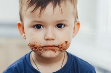 Charming child portrait, dirty face in chocolate or condensed milk
