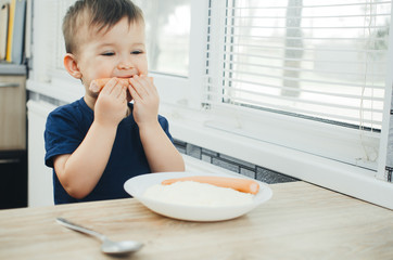 baby eating sausage in the kitchen is very charming and emotional